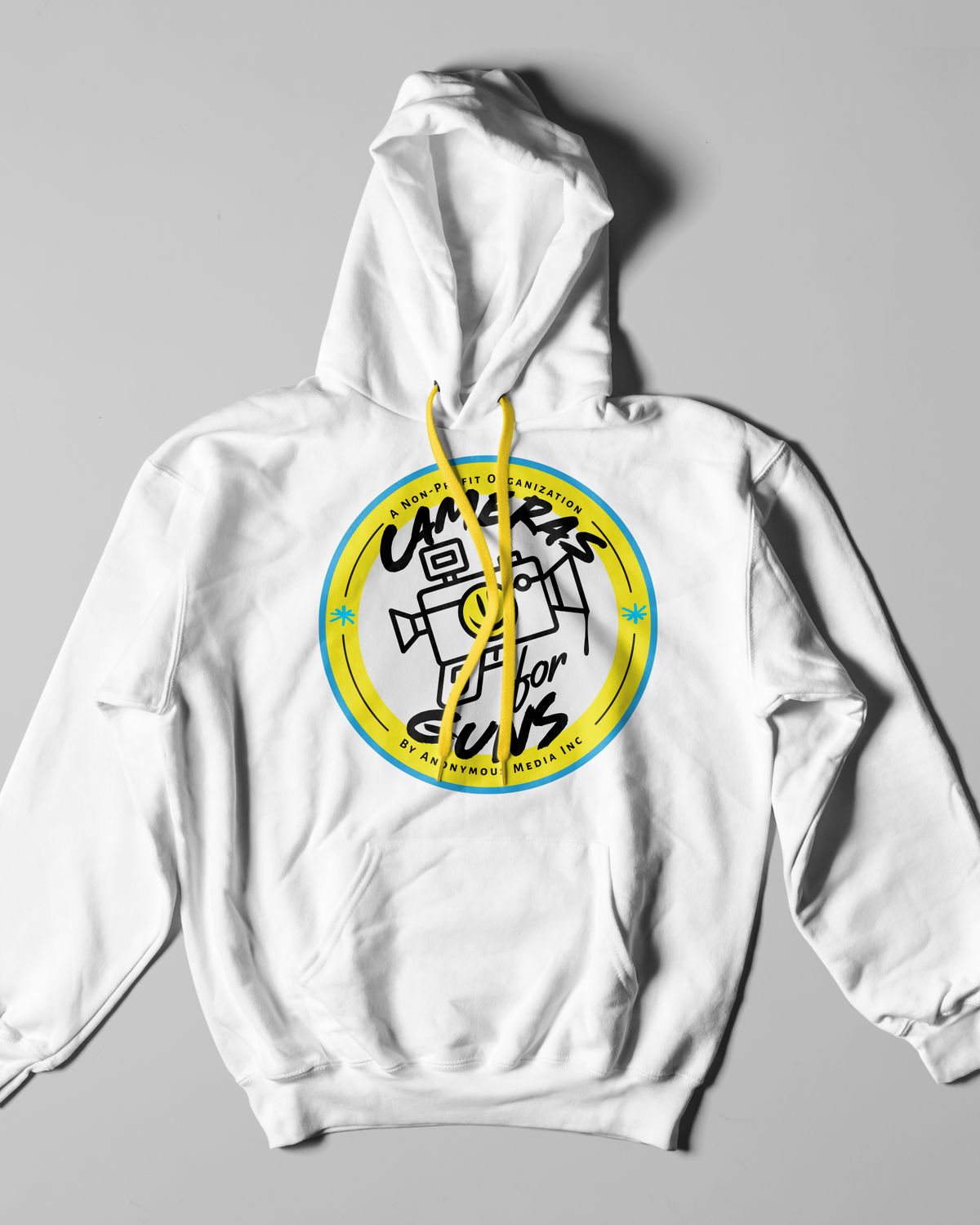 White hoodie with yellow drawstrings and the Cameras for Guns badge on the chest, laid flat